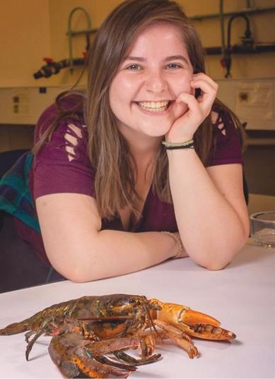 一位英国东北大学的学生坐在一只龙虾旁边微笑着